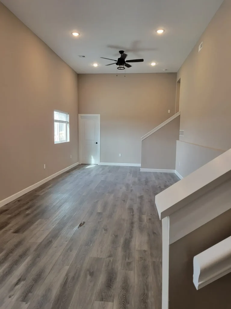 Empty living room with hardwood floors and a ceiling fan.